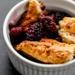 Close up front view of single serving of blackberry cobbler in small white bowl.
