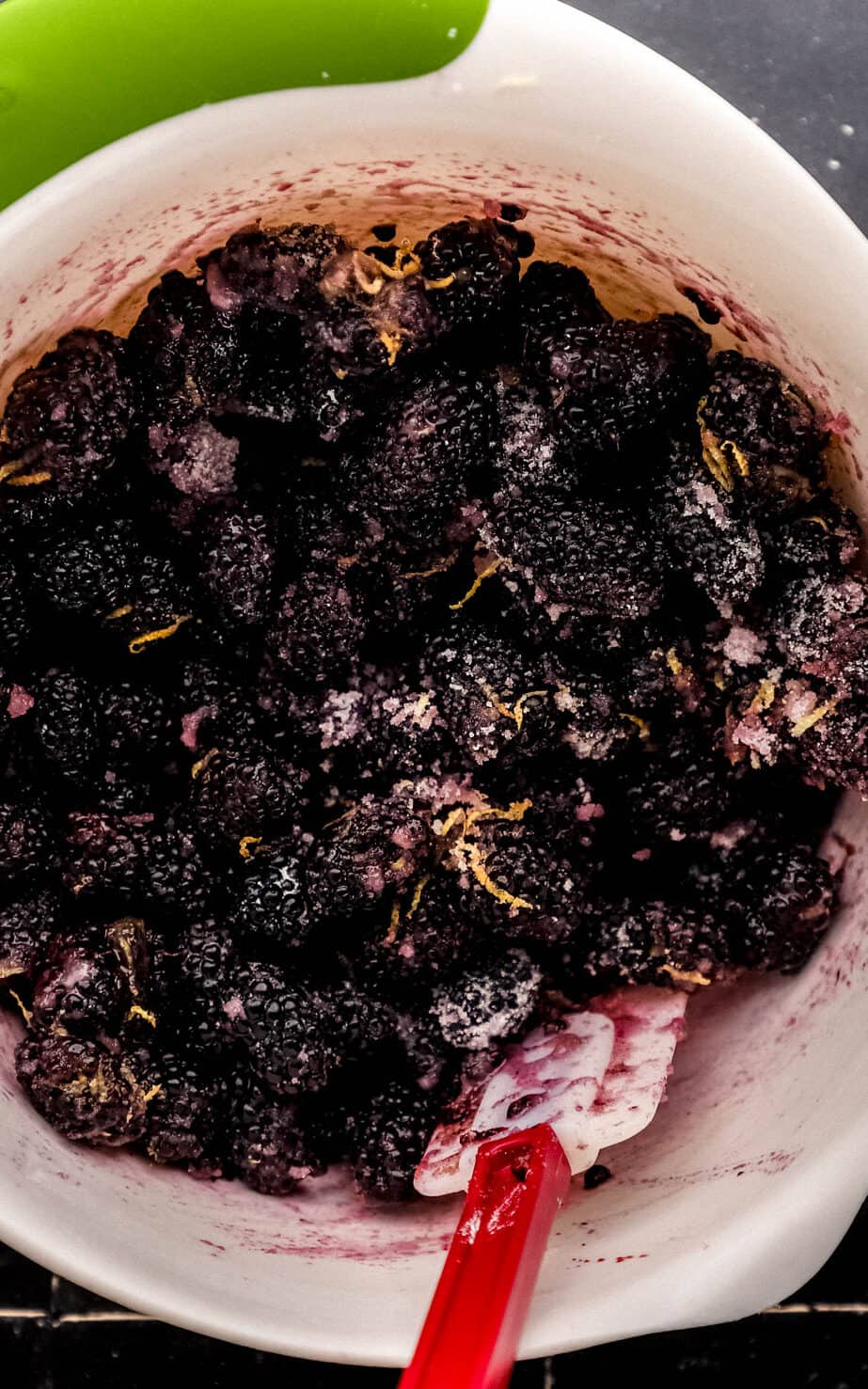 Blackberry cobbler filling ingredients combined in white mixing bowl with spatula. 
