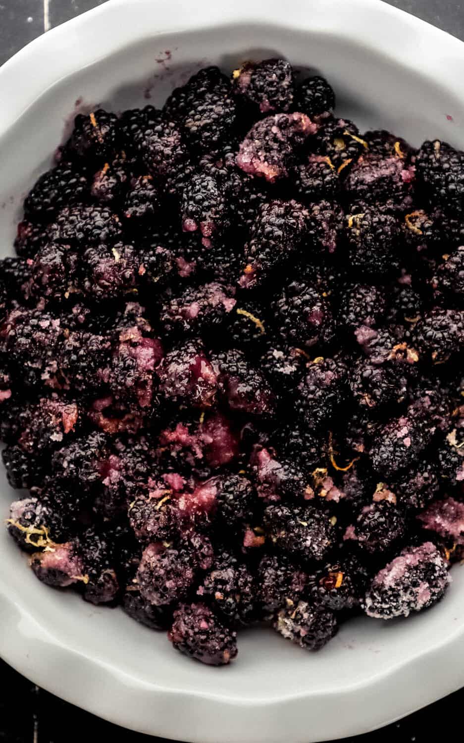 Overhead view of blackberry filling mixture added to round white baking dish. 