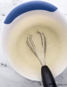 Overhead view of glaze ingredients combined in mixing bowl with whisk.