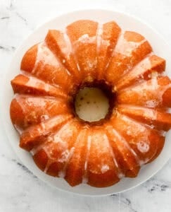 Overhead view of glazed added to cake on white plate.