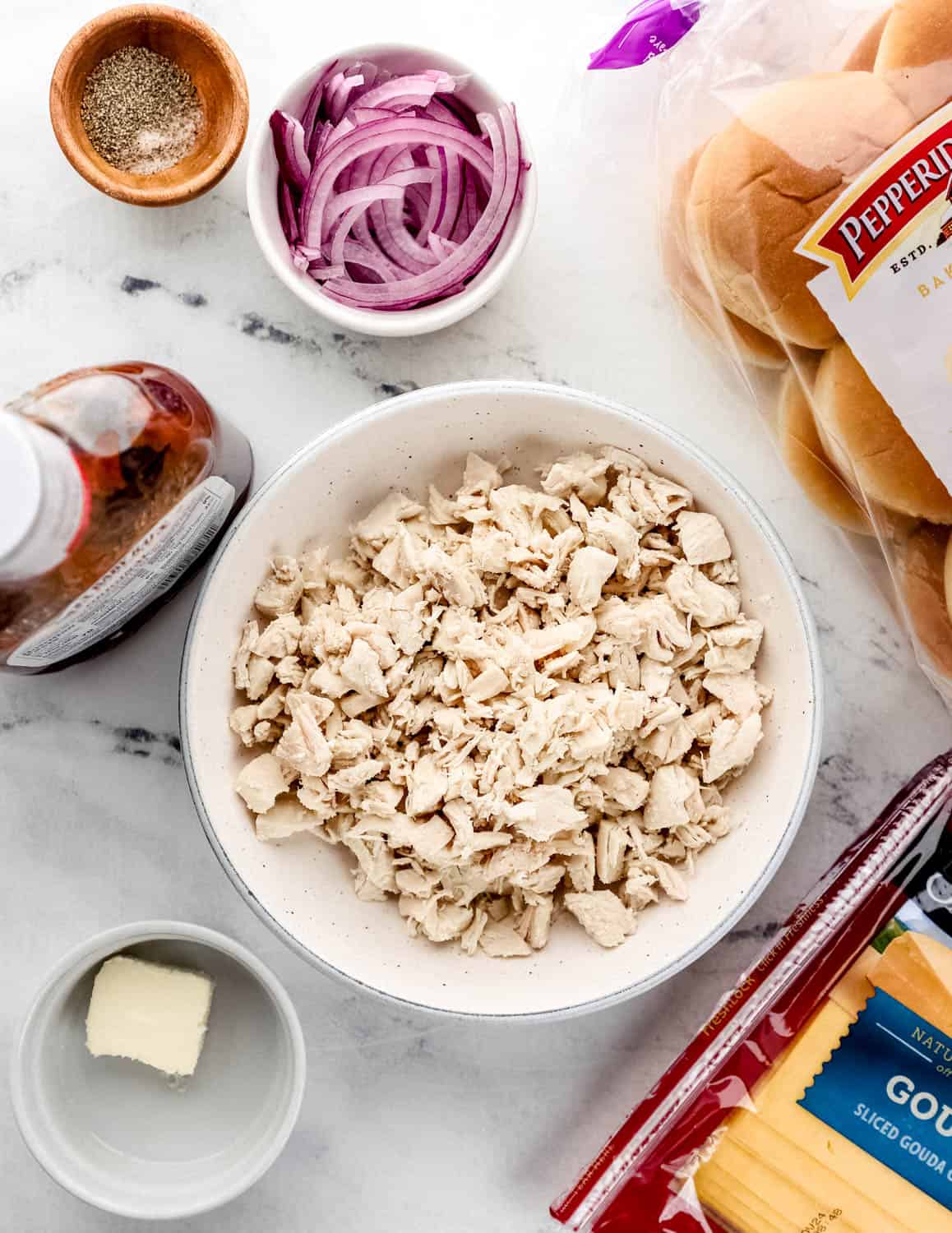Overhead view of ingredients needed to make sliders in separate bowls and containers on marble surface. 