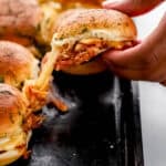 Close up front view of sliders on sheet pan with hand pulling on of them.