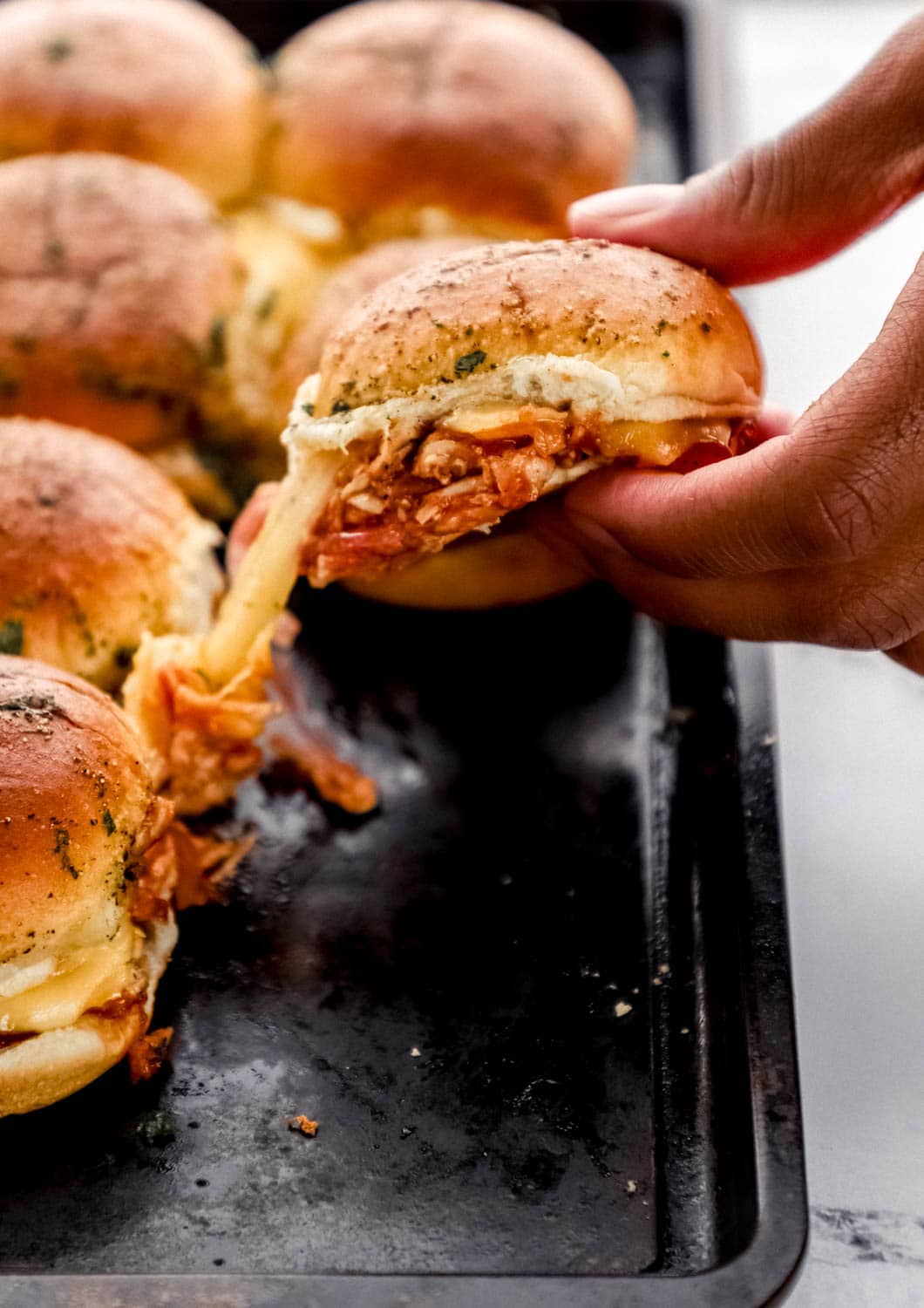 Close up view of hand pulling single slider on top of baking sheet. 