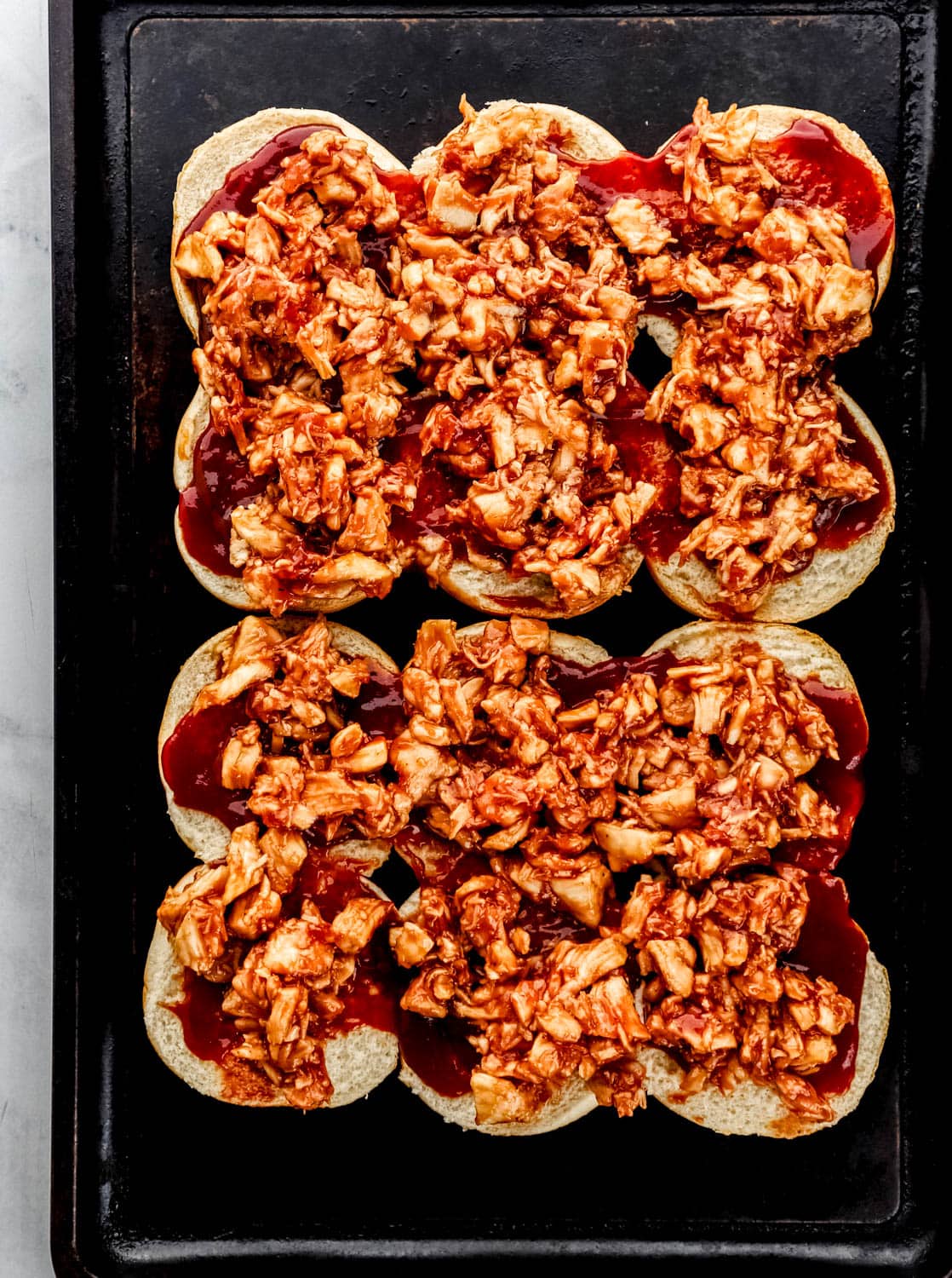 Bottom half of slider buns topped with sauce and barbecue chicken. 