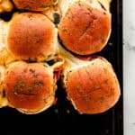 Overhead view of bbq chicken sliders on sheet pan with some pulled apart from the rest.