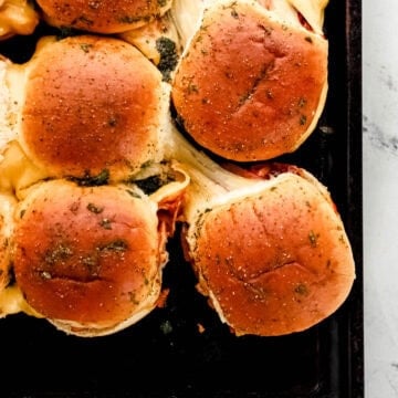 Overhead view of bbq chicken sliders on sheet pan with some pulled apart from the rest.