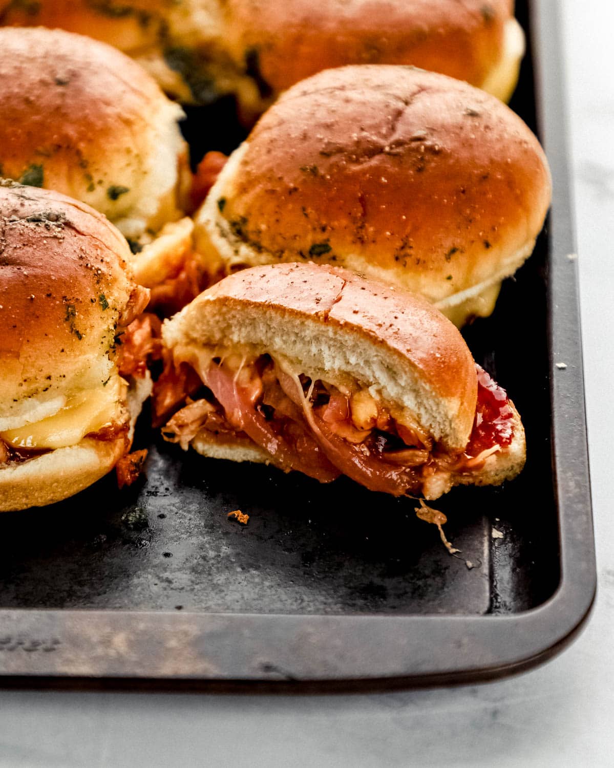 Close up front view of finished sliders on baking sheet with one cut in half. 