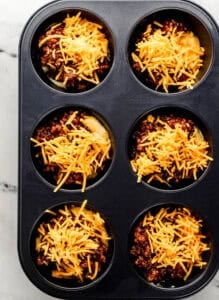 Shredded cheese added to the other ingredients in the muffin pan.