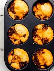 Close up overhead view of finished muffins in muffin pan on marble surface.