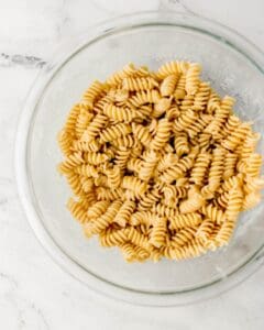 Overhead view of pasta and dressing in mixing bowl.