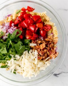 Pasta salad ingredients in large glass mixing bowl.