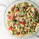 Overhead view of finished pasta salad in large glass mixing bowl.
