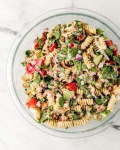 Overhead view of finished pasta salad in large glass mixing bowl.
