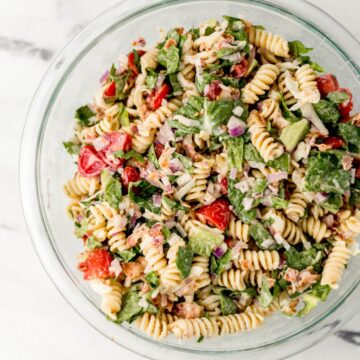Overhead view of finished pasta salad in large glass mixing bowl.