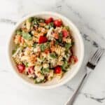 Overhead view of serving of finished salad in white bowl by a fork on marble surface.