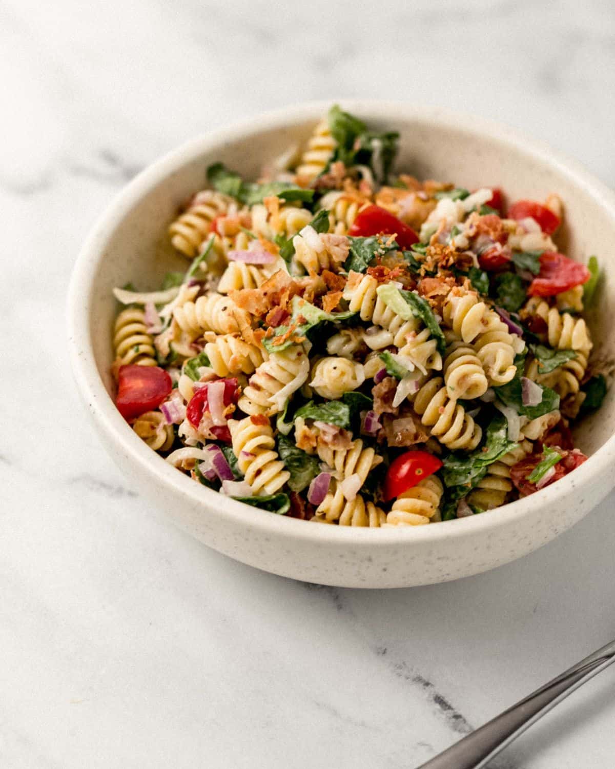 Close up view of serving of pasta salad in white bowl on marble surface. 