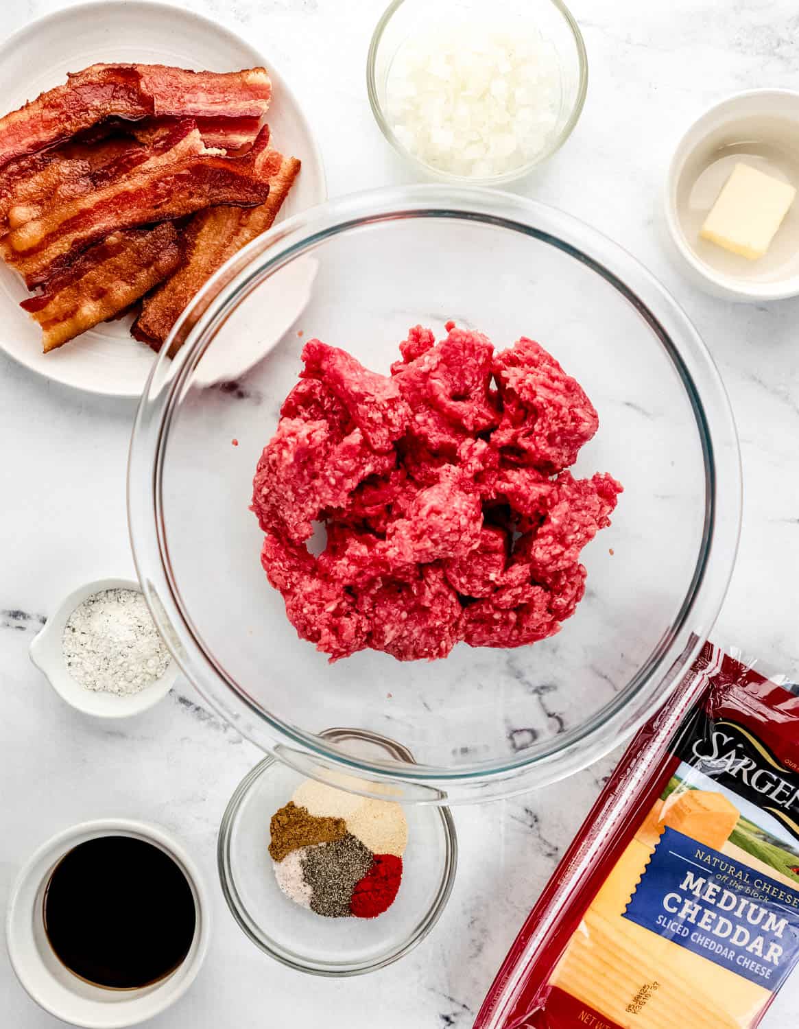 Overhead view of ingredients needed to make sliders in separate bowls on marble surface. 