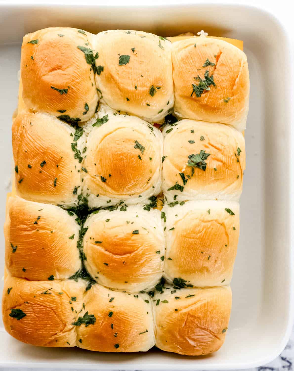 Tops of buns added to the other slider ingredients in white baking dish. 