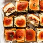 Overhead view of cheeseburger sliders in parchment lined baking dish.
