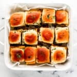 Overhead view of finished sliders in parchment lined baking dish on marble surface.