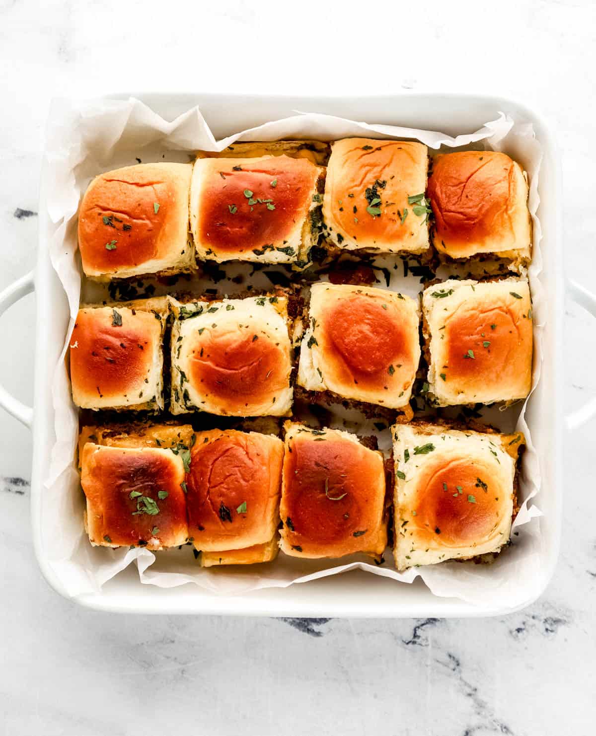 Overhead view of individually cut sliders in parchment lined baking dish. 