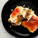 Overhead view of two sliders on black plate with one having a bite in it.