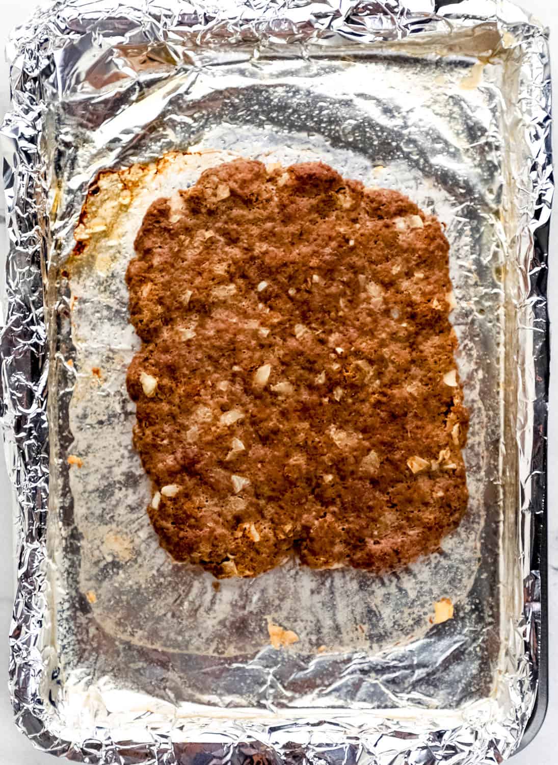 Overhead view of beef patty on aluminum foil lined baking sheet. 