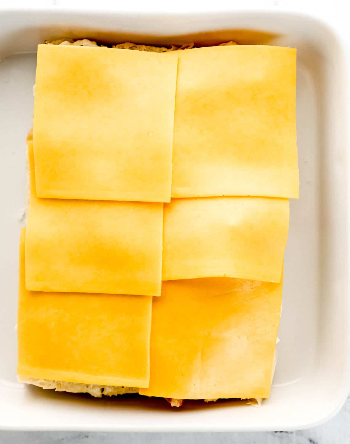 Sliced cheese added to sliders in white baking dish. 