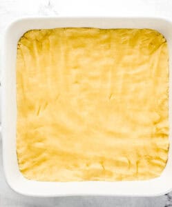Overhead view of crust layer of squares added to the bottom of a baking dish.