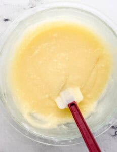 Second layer ingredients added to glass mixing bowl with spatula.