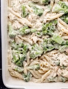 Overhead view of sauce added to pasta and broccoli in baking dish.
