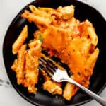 Overhead view of black plate with single serving of pasta on it with a fork in it.