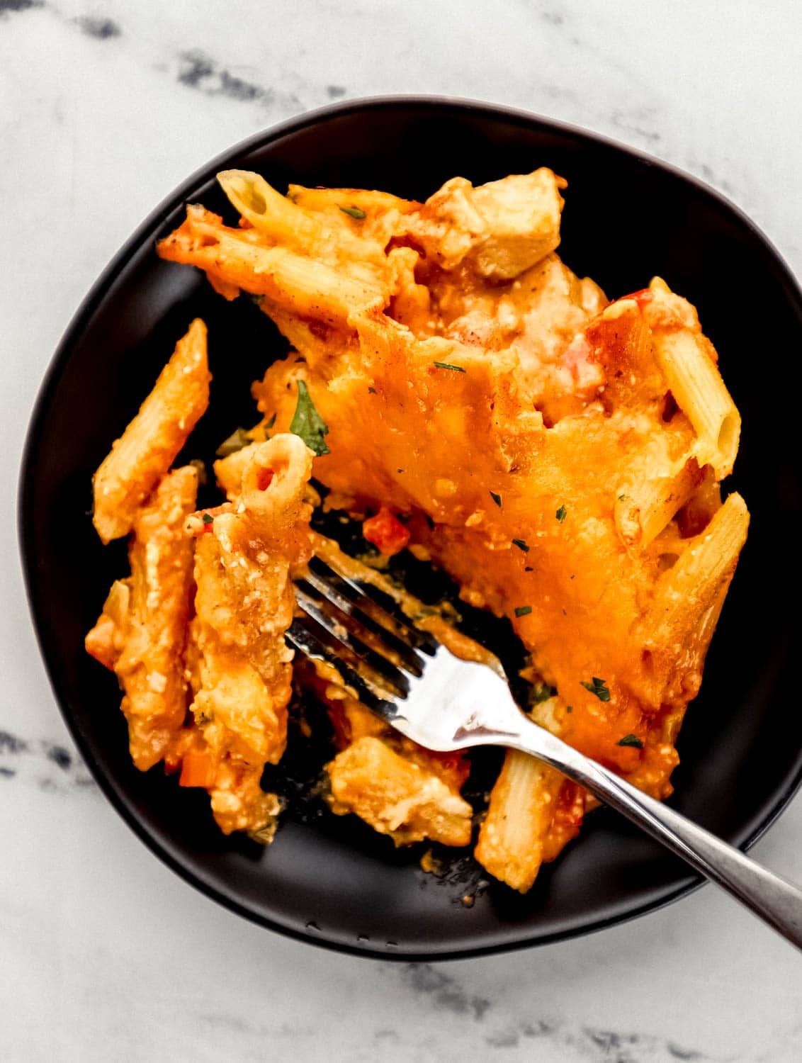 Overhead view of black plate with single serving of finished pasta on it with for in it.