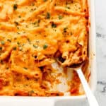 Close up front view of baked pasta in white casserole dish with serving spoon in it.