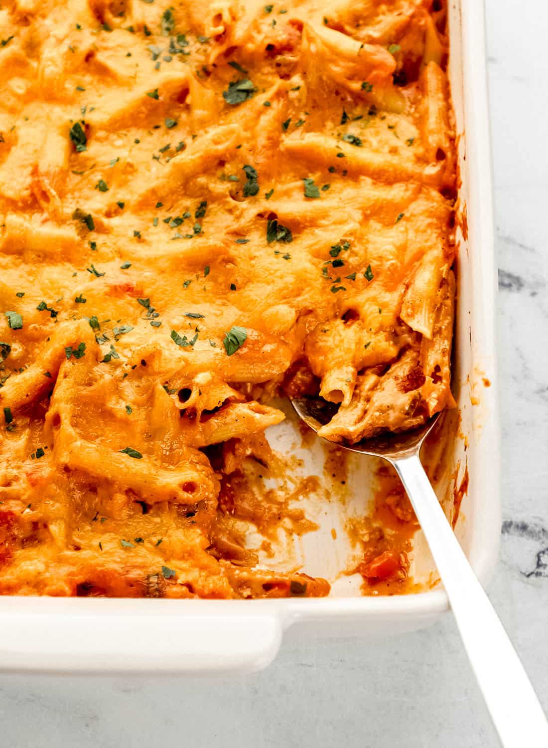 Close up front view of finished pasta bake in baking dish with serving spoon in it.