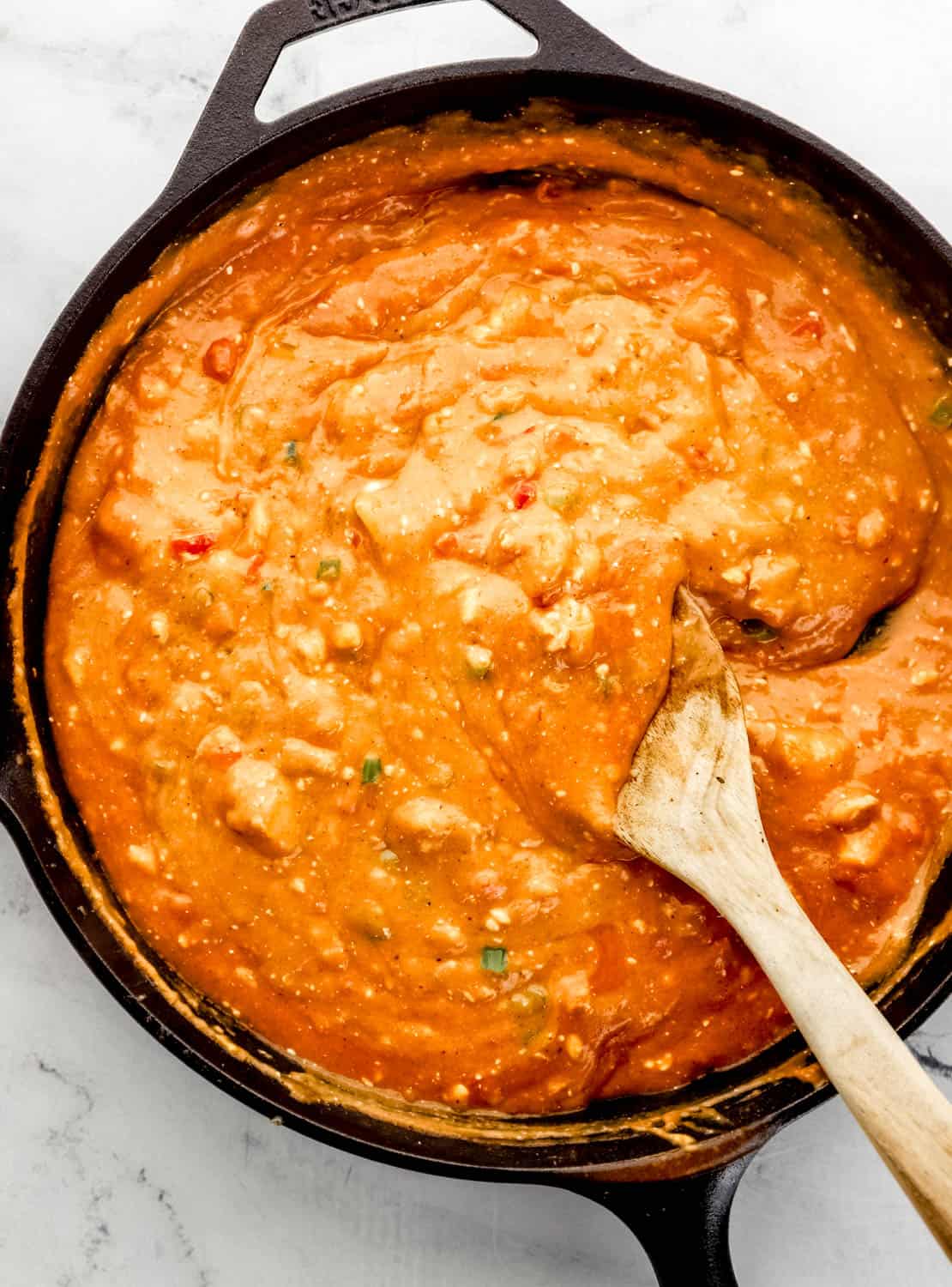 Pasta sauce in cast iron skillet with wooden spoon in it on marble surface.