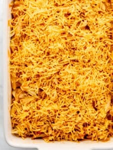 Shredded cheese added to pasta in white baking dish.