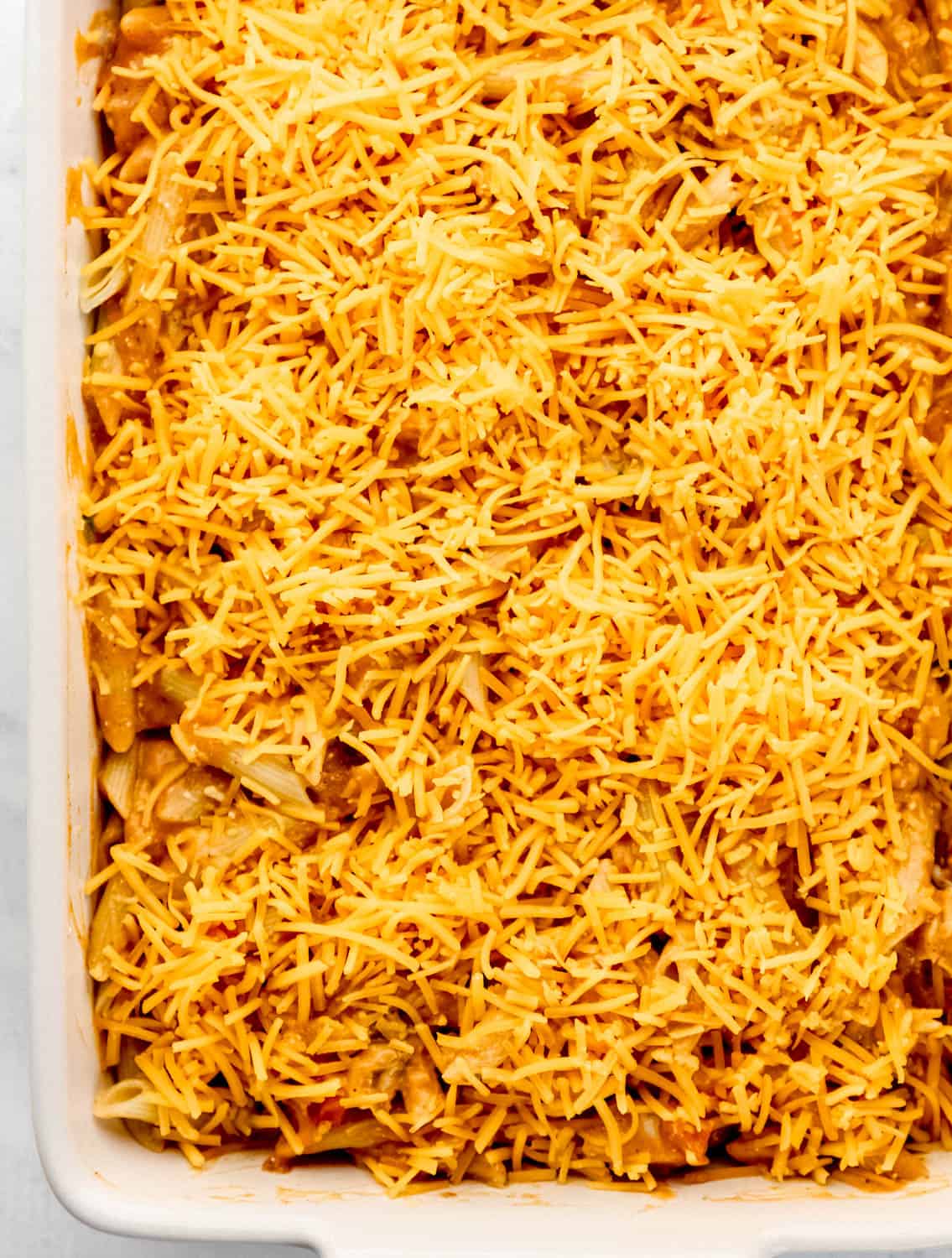 Close up overhead view of pasta in casserole dish topped with shredded cheese.
