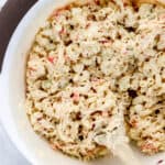 Overhead view of large white mixing bowl with pasta salad and wooden spoon in it.