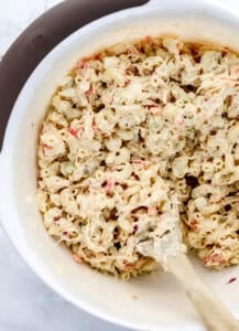 Overhead view of large white mixing bowl with pasta salad and wooden spoon in it.