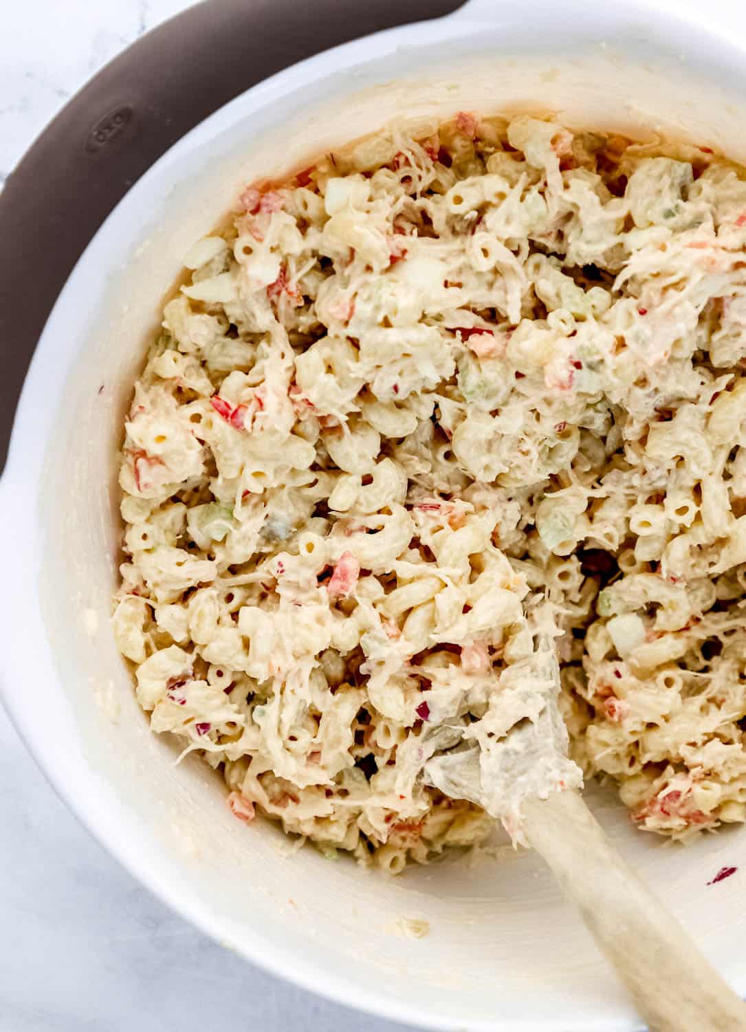 Macaroni pasta added to mixing bowl with wooden spoon and other pasta ingredients. 