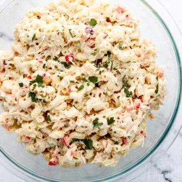 Overhead view of macaroni salad in large glass bowl topped with fresh chopped parsley.