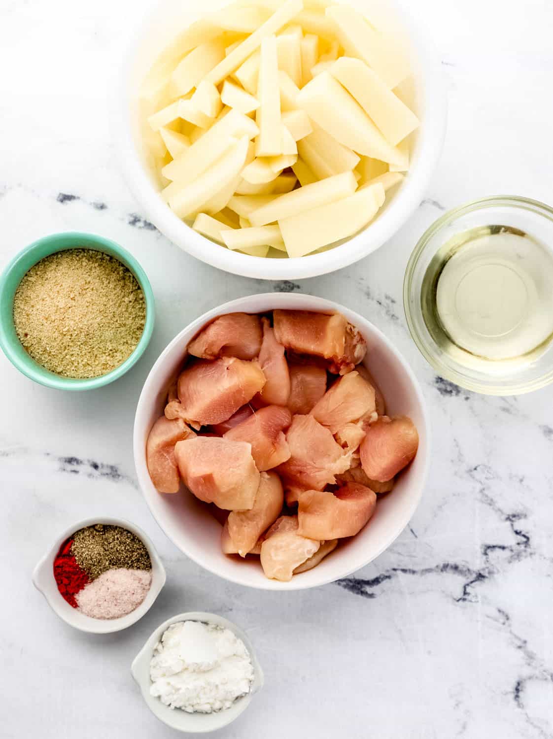 Overhead view of ingredients needed to make nuggets and fries in separate bowl on marble surface. 
