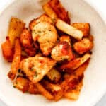 Close up view of white bowl with chicken nuggets and fries in it topped with parsley.