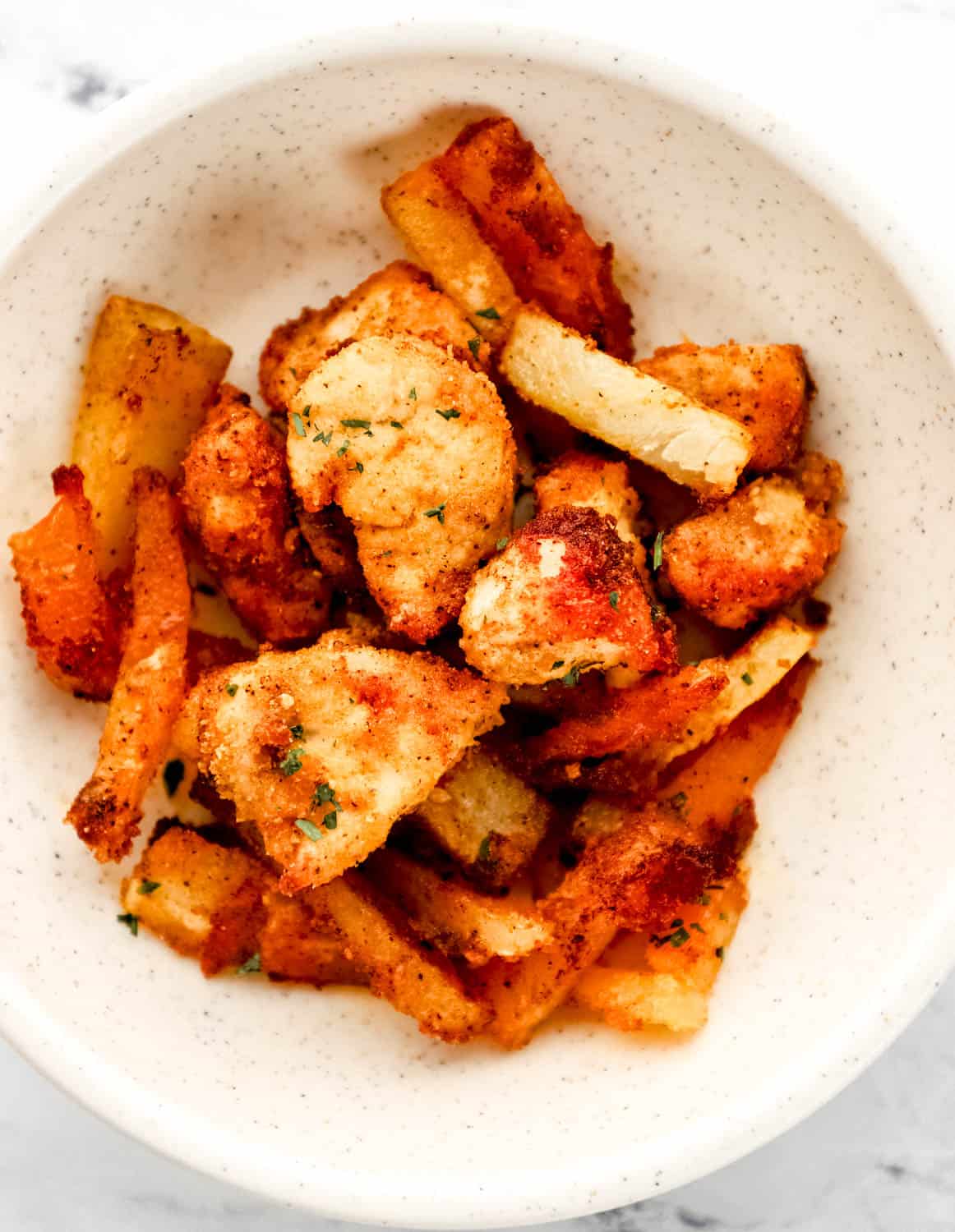 Close up view of chicken and potatoes in white bowl topped with freshly chopped parsley. 