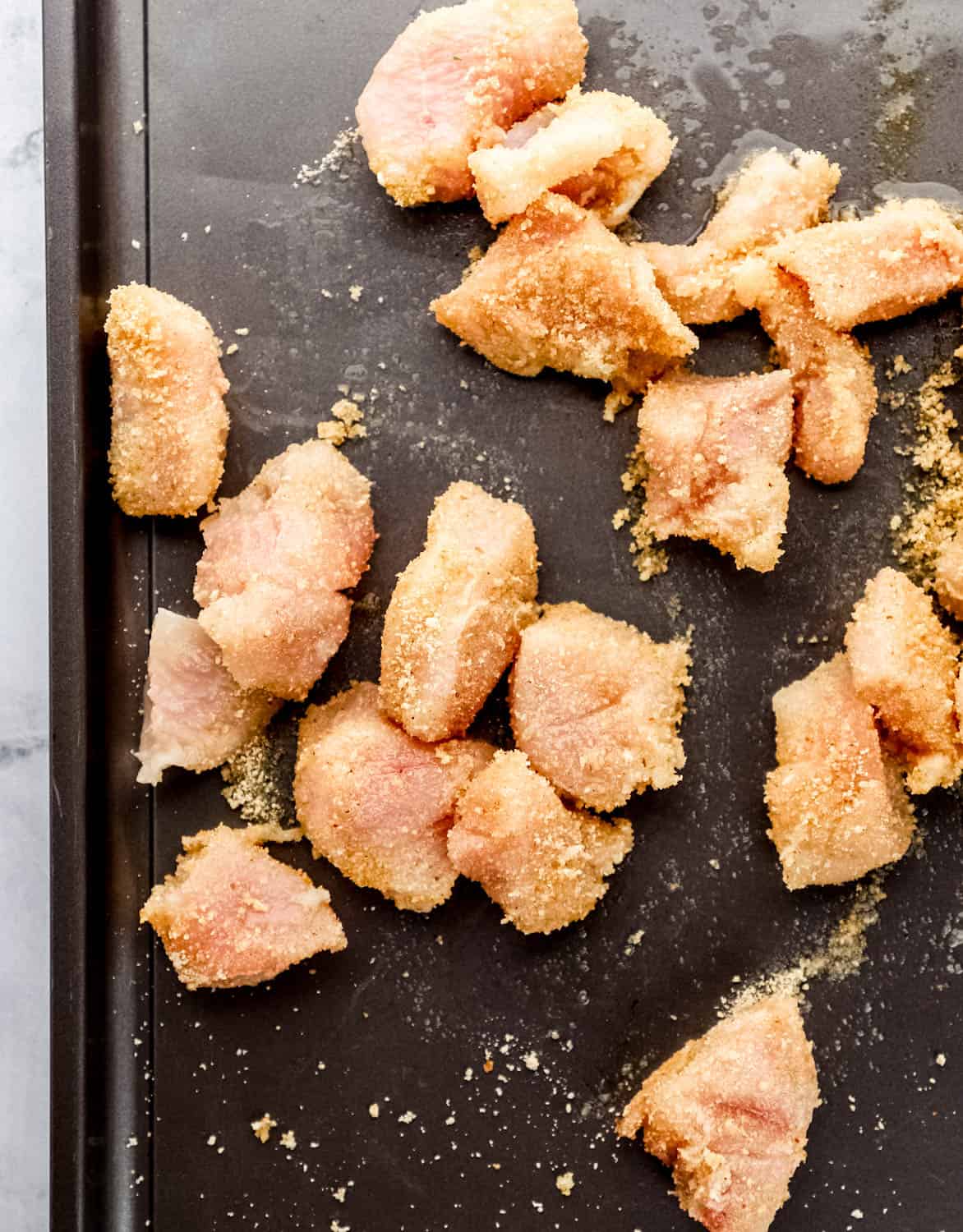 Chicken coated in oil and breadcrumbs on sheet pan. 