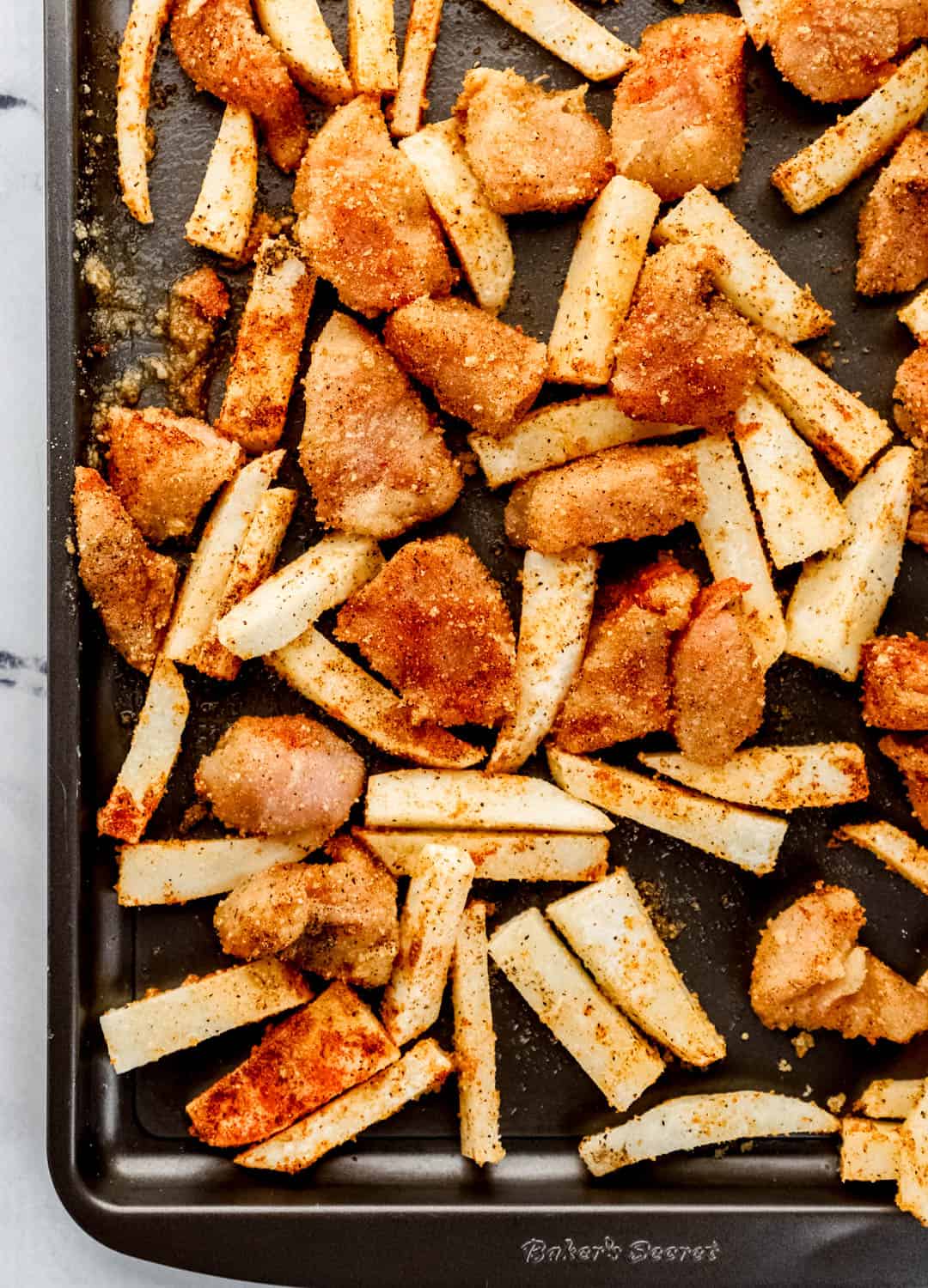 Overhead view of seasoned chicken and potatoes on sheet pan before baking. 