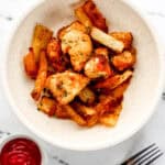 Overhead view of white bowl with nuggets and fries in it by a small bowl of ketchup and fork.