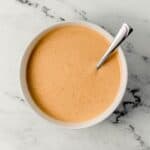Overhead view of sauce ingredients combined in white bowl with spoon.